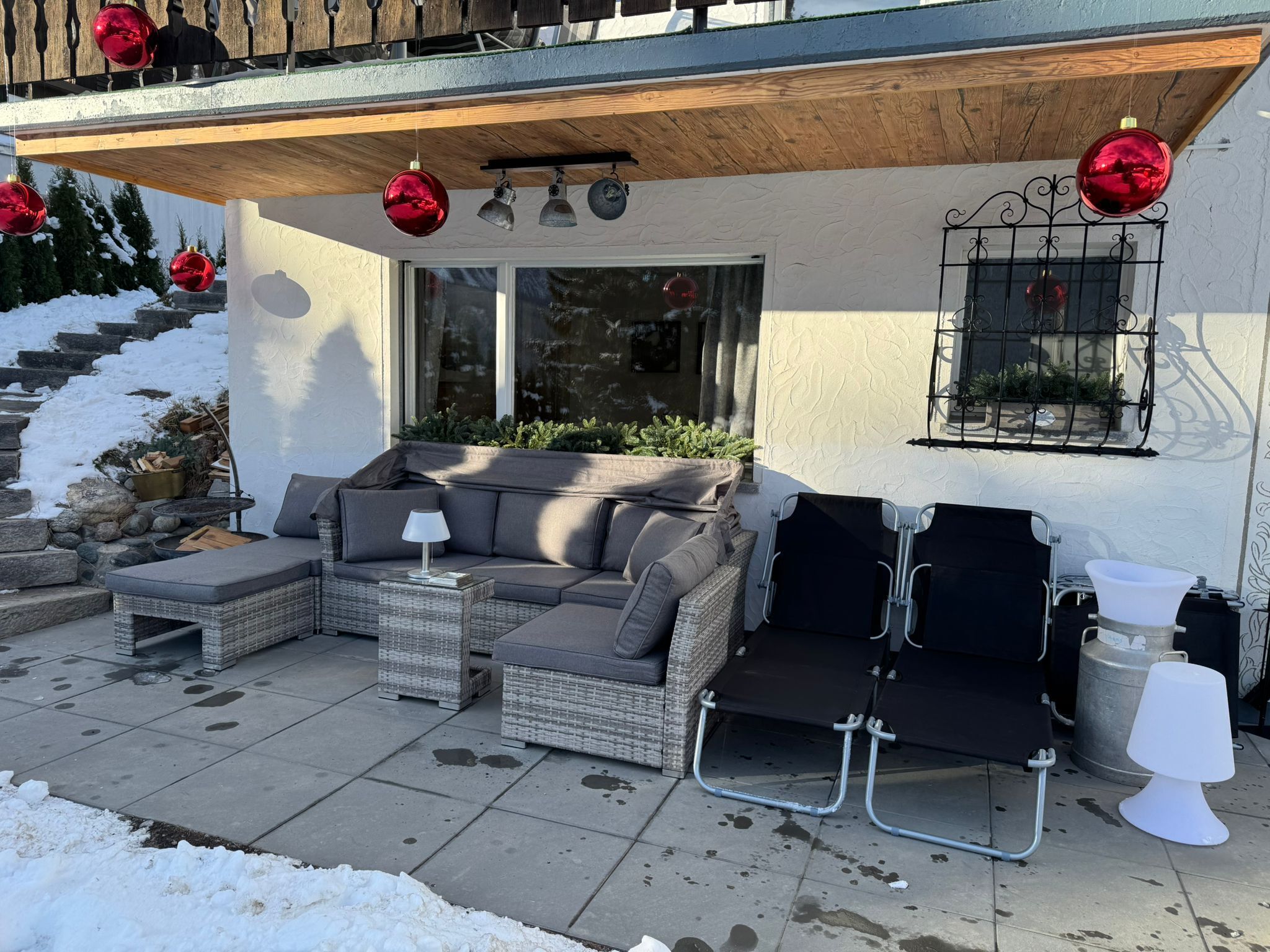 An outdoor seating area with a sofa, two chairs, a table, and a lamp.