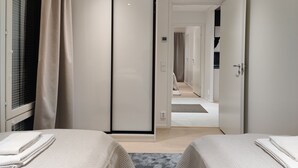 A hotel room with a sliding door closet, two beds with towels, a window with curtains, and a hallway leading to another room. - Serviced Apts Rovaniemi Willamonkuja (Rovaniemi)
