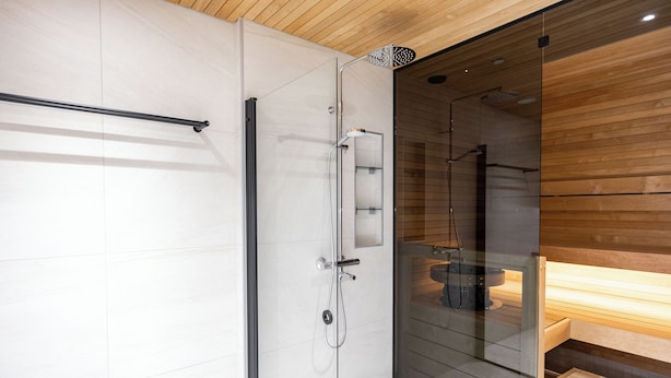 A modern bathroom with a glass shower enclosure, a wooden bench, and a visible toilet. - Serviced Apts Rovaniemi Willamonkuja (Rovaniemi)