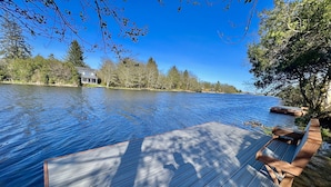 A wooden dock extending into a calm lake with a house in the background. - True Luxury Waterfront: Dock, Kayaks & Hot Tub (Ocean Shores)