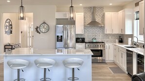 A modern kitchen with a central island, bar stools, stainless steel appliances, and pendant lighting. - True Luxury Waterfront: Dock, Kayaks & Hot Tub (Ocean Shores)