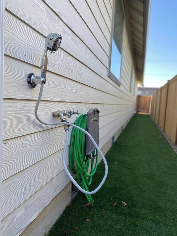 Vue de côté d’une maison, avec un tuyau d’arrosage raccordé à un robinet extérieur sur le mur.