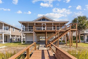 A beachfront property with a wooden deck leading to a house with a covered porch and a staircase.