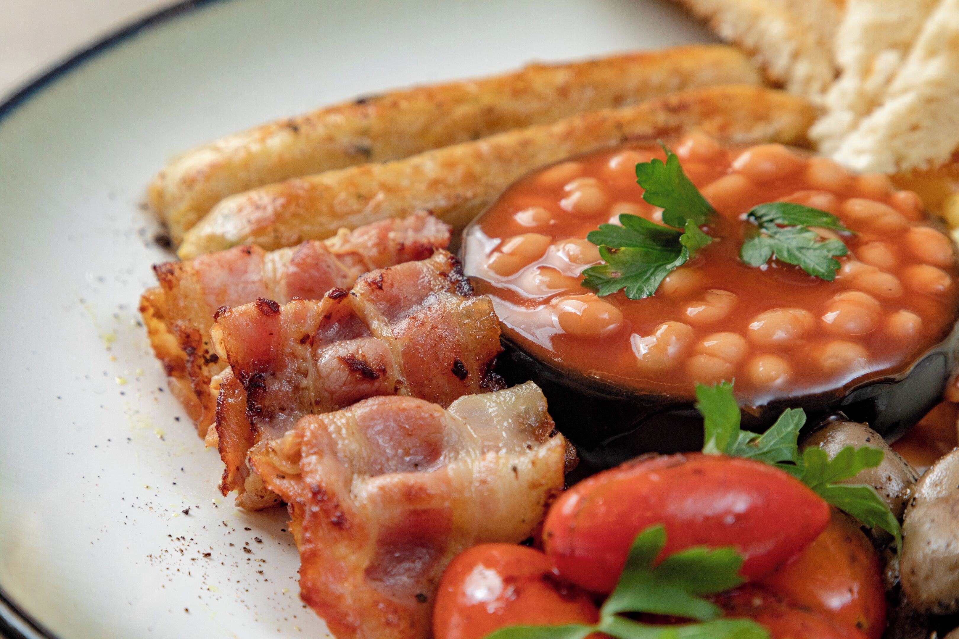 A plate with bacon, baked beans, tomatoes, and bread.