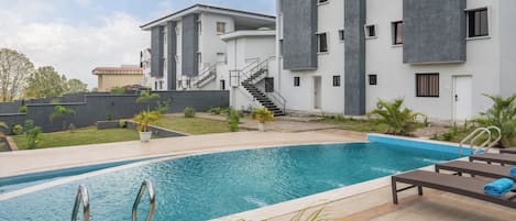 A modern residential building with a swimming pool, outdoor seating, and a well-maintained garden.