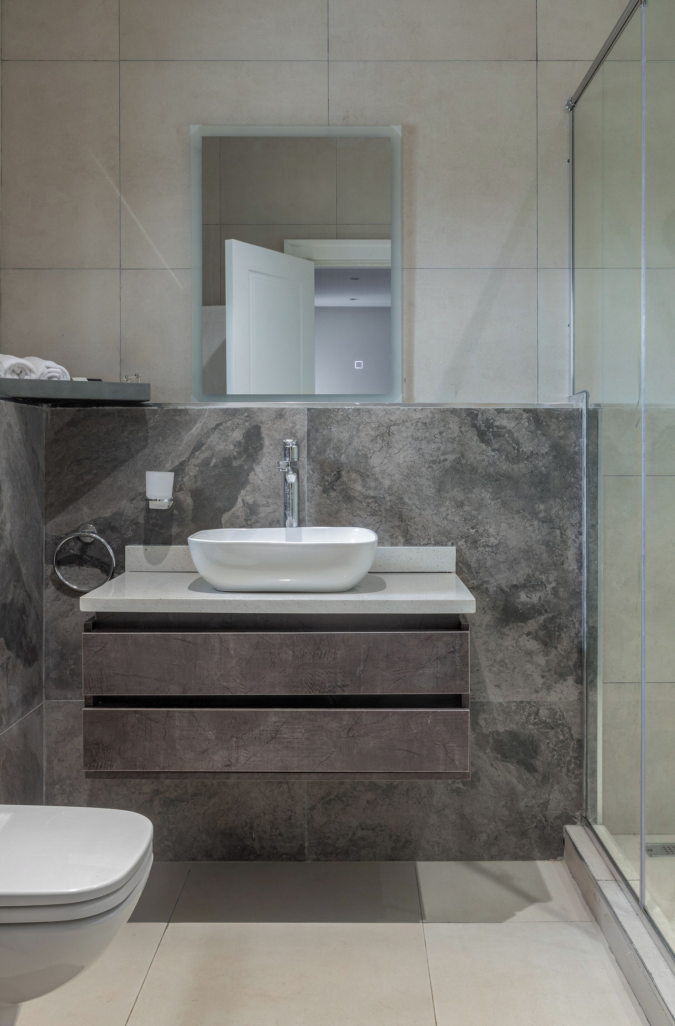 A modern bathroom with a white sink, dark marble walls, and a glass shower enclosure.