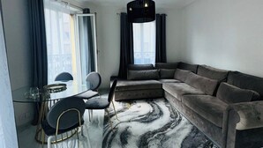 Una sala de estar moderna con un sofá modular, un comedor con mesa de vidrio y un ventanal con cortinas.