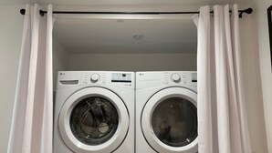 Une buanderie équipée de deux machines à laver à chargement frontal et d’un sèche-linge, le tout séparé par des rideaux blancs.