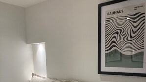 Un lit bien fait, avec du linge de lit blanc et des oreillers, une œuvre d’art encadrée au mur et une lampe de chevet.