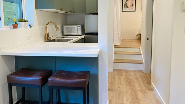 Une cuisine moderne avec un plan de travail blanc, deux tabourets, un four à micro-ondes et un évier.