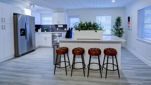 Una cuina moderna amb armaris blancs, un frigorífic d'acer inoxidable, una illa central amb tamborets i una planta en test.