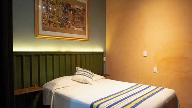 Une chambre d’hôtel avec un lit, un tableau encadré au mur et un luminaire au plafond.