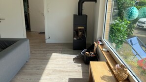 A compact living space with a sofa, a small wooden table, a black heater, and a window with a view of a car and greenery outside.