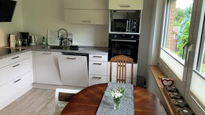 A modern kitchen with white cabinets, a built-in oven, and a microwave. There's a dining table with a patterned table runner and a vase of flowers.
