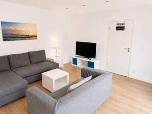 A modern living room with a grey sofa, a white coffee table, and a flat-screen TV on a blue and white stand.