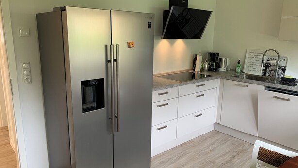 A modern kitchen with a stainless steel refrigerator, white cabinets, a built-in oven, and a sink with a faucet.