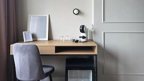 A small, neatly organized workspace with a desk, chair, and a glass-fronted cabinet containing bottles. - Corso Italia Rooms (Milan)