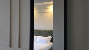 A mirror reflecting a neatly made bed with white linens and a green headboard in a room with white walls and wooden flooring. - Corso Italia Rooms (Milan)