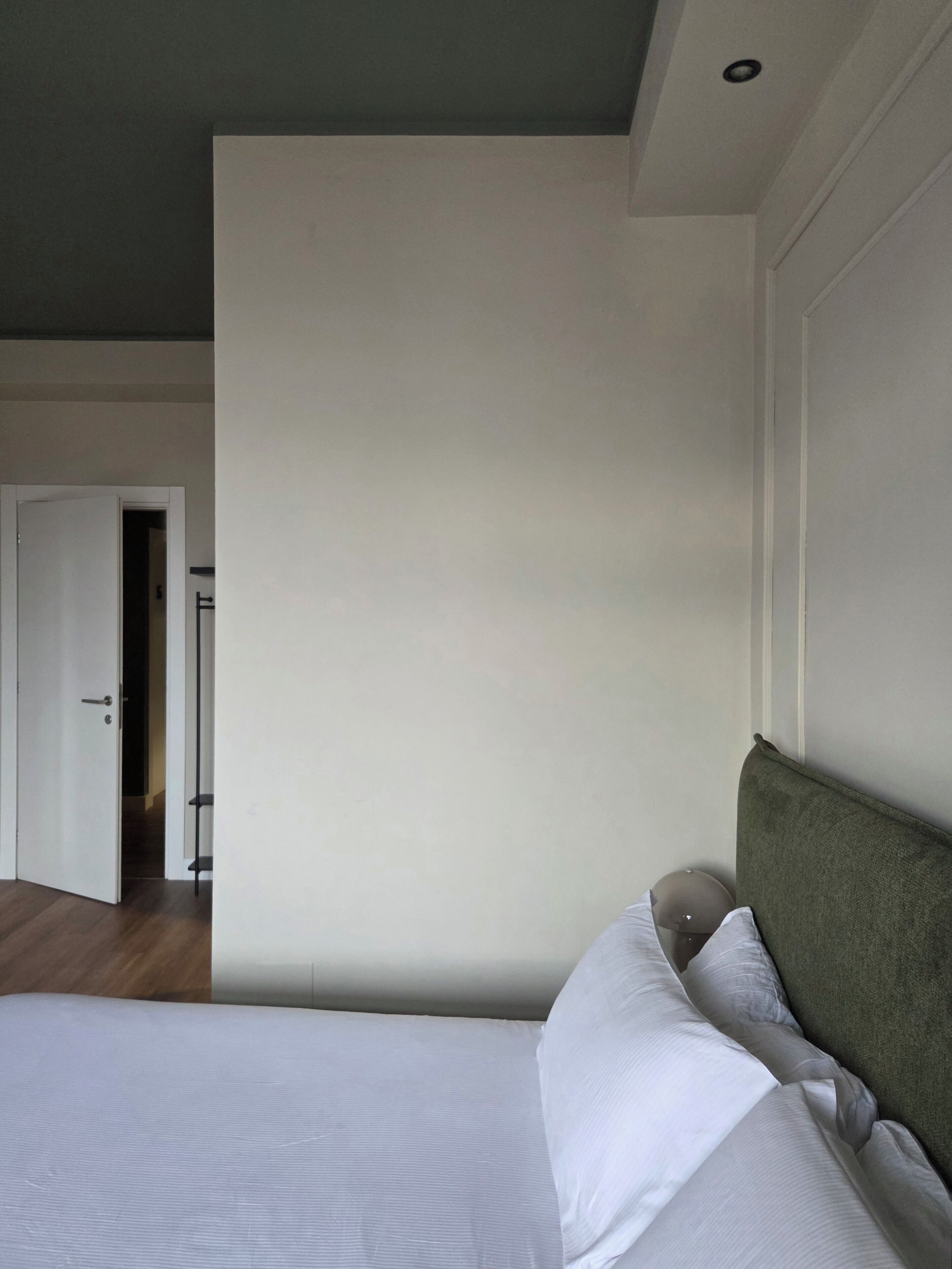 A bedroom with a bed, a door, and a view of another room.