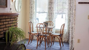 A dining area with a brick fireplace, a table with six chairs, and a view through patterned curtains. - Charming, Unique and Peaceful 3-bedroom Farmhouse on 500 acres in Great Bend, PA (Great Bend)