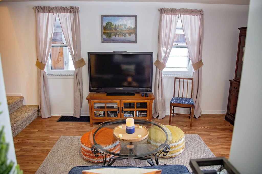 A living room with a flat-screen TV, wooden cabinet, glass coffee table, and a chair.