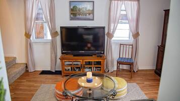 A living room with a flat-screen TV, wooden cabinet, glass coffee table, and a chair.