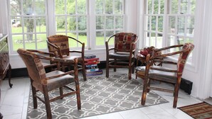 Une pièce lumineuse, baignée de soleil, avec de grandes fenêtres, des chaises en bois, un tapis à motifs et une bibliothèque remplie de livres.