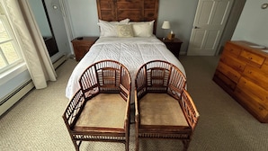 A bedroom with a large bed, two wicker chairs, a wooden dresser, a nightstand, and a door. - The Bond Inn Room #7 (Warrensburg)