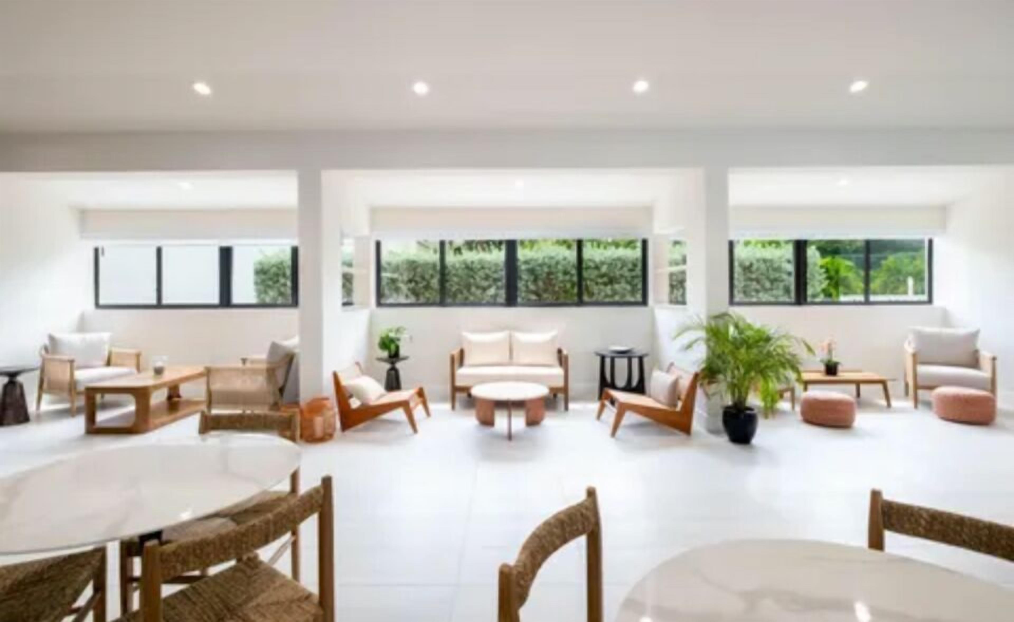 A spacious, well-lit room with large windows, a central seating area with a sofa and chairs, and a dining table with chairs.