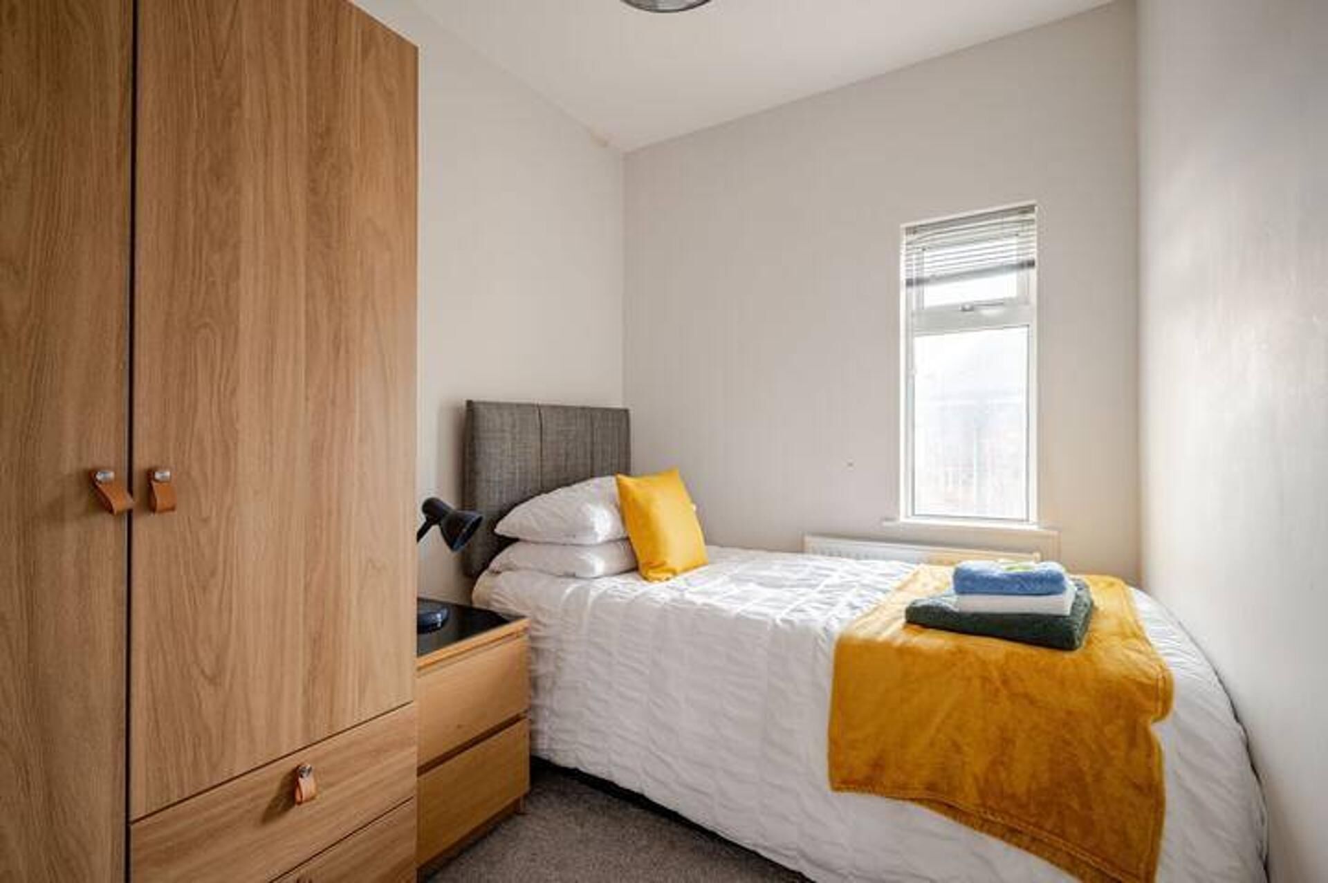 A bedroom with a bed, a nightstand, a wardrobe, and a window.