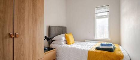 A bedroom with a bed, a nightstand, a wardrobe, and a window.
