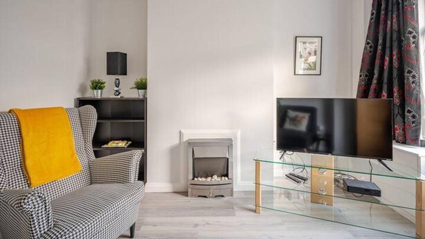Un salon avec un canapé, une cheminée, un téléviseur posé sur un meuble en verre et une fenêtre avec des rideaux.