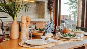 Una mesa de comedor preparada con platos, vasos y un florero con plantas secas.