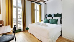 Une chambre d’hôtel avec un lit, une chaise, une table et de grandes fenêtres avec des rideaux.