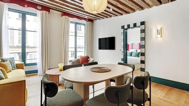 Un salon moderne avec une table ronde, des sièges confortables, un téléviseur à écran plat et une grande fenêtre avec des rideaux.