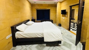 A hotel room with a bed, a ceiling fan, a TV mounted on the wall, and a window with curtains. - Hotel Rainbow Jaisalmer (Jaisalmer)