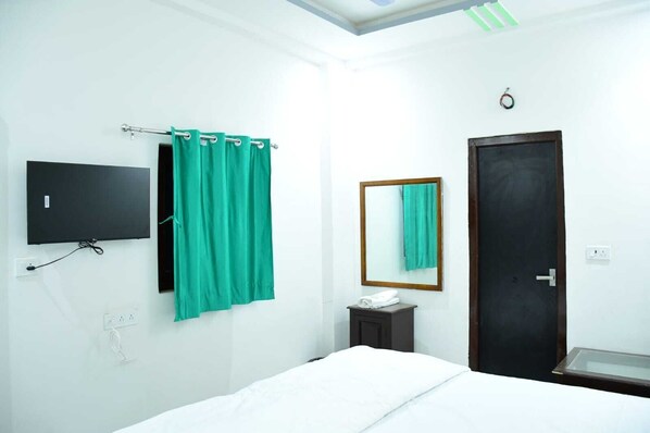A hotel room with a bed, a TV mounted on the wall, a bathroom with a mirror, and a door. - Hotel Rainbow Jaisalmer (Jaisalmer)