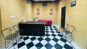 A room with a checkered floor, a central table with a red tablecloth, and two metal chairs. - Hotel Rainbow Jaisalmer (Jaisalmer)