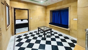 A room with a checkered floor, bunk beds, a small table, and a window with curtains. - Hotel Rainbow Jaisalmer (Jaisalmer)