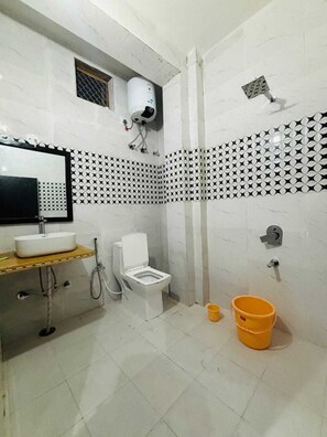 Un baño con lavamanos, inodoro y zona de ducha blancos. Hay un espejo sobre el lavamanos y una pared con un diseño decorativo.
