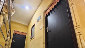 A hallway with a checkered floor, two dark doors with decorative trim, and a metal staircase on the left. - Hotel Rainbow Jaisalmer (Jaisalmer)