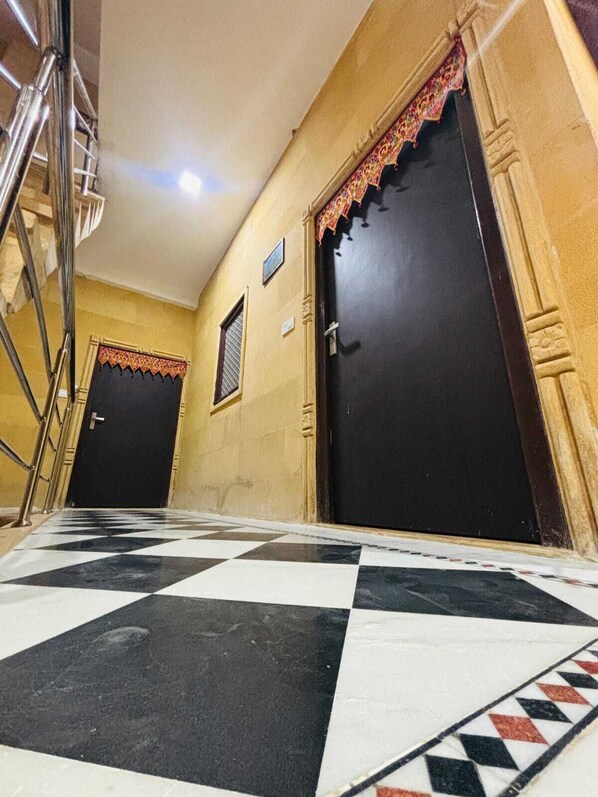 A hallway with a checkered floor, two dark doors with decorative trim, and a metal staircase on the left. - Hotel Rainbow Jaisalmer (Jaisalmer)