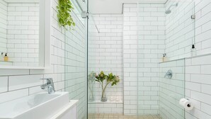 A modern bathroom with white tiles, a glass shower enclosure, a sink, and a toilet. - Apartment Seacliff - Two Bedroom Apartment, Sleeps 4 (Cape Town)