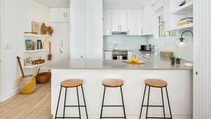 A modern kitchen with white cabinets, a central island with stools, and a variety of kitchen appliances. - Apartment Seacliff - Two Bedroom Apartment, Sleeps 4 (Cape Town)