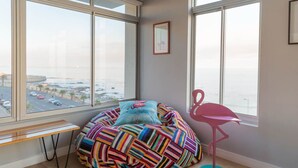 Ein Zimmer mit Sitzsack, rosa Stuhl und Blick auf eine Stadtlandschaft durch große Fenster.