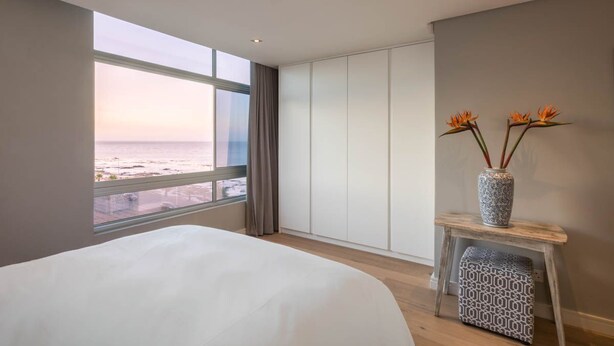 Ein Schlafzimmer mit einem großen Bett, Meerblick, einer Blumenvase und einem kleinen Tisch.