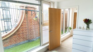 Een kamer met een groot raam, een bakstenen muur, een witte dressoir en een houten deur.