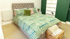 Een net opgemaakt bed met gestreept beddengoed, een gestoffeerd hoofdbord en een klein nachtkastje met een plantje.