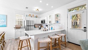 Una cocina moderna con armarios blancos, una isla central con taburetes, un refrigerador y un microondas.