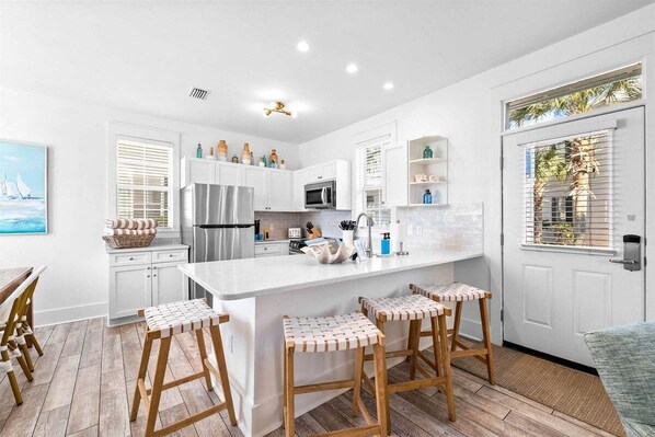 A modern kitchen with white cabinetry, a central island with stools, a refrigerator, and a microwave.